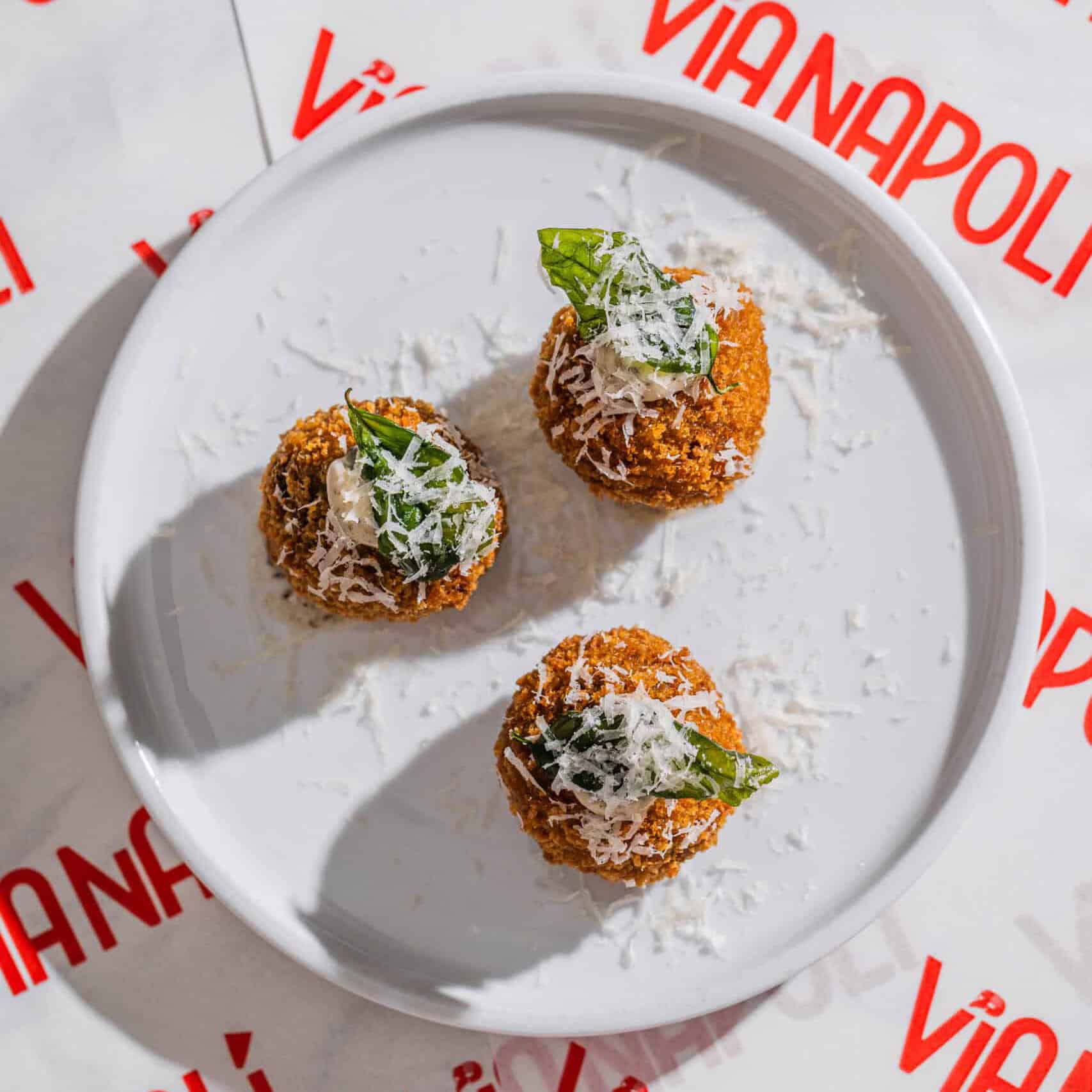 Golden-brown arancini balls topped with shaved Parmigiano Reggiano, creamy truffle sauce, and crispy basil leaves