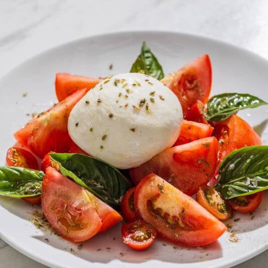 Creamy burrata cheese served with fresh tomatoes, basil leaves, and a drizzle of extra virgin olive oil