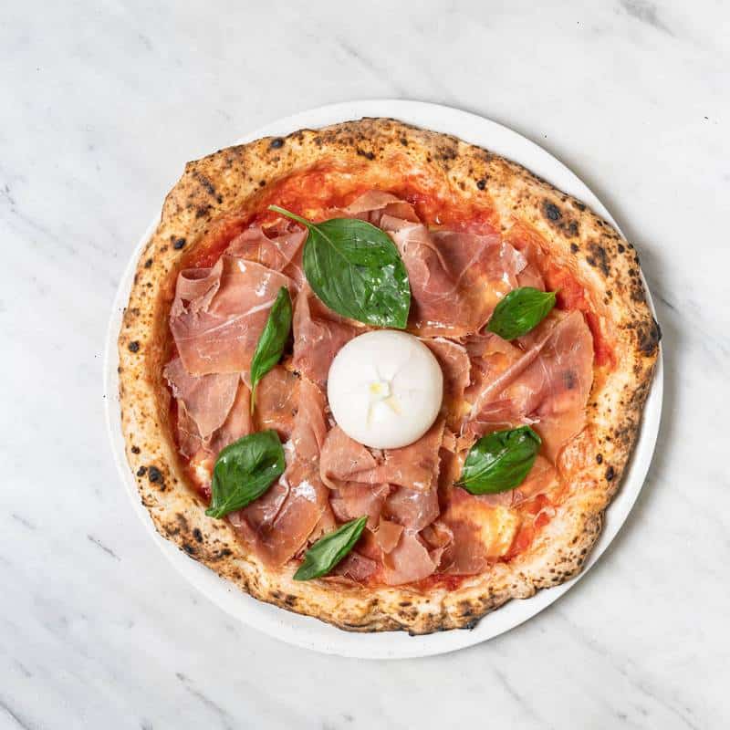 Burratina pizza topped with fior di latte, San Marzano tomato, Prosciutto di Parma, creamy burrata cheese, and cracked pepper