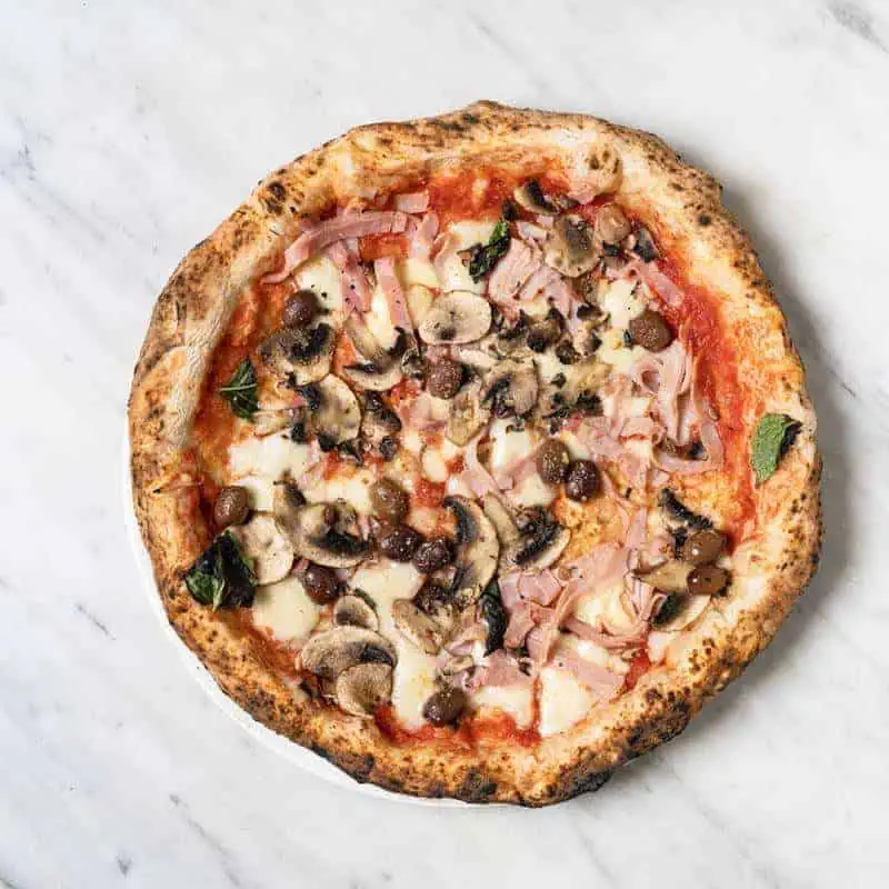 Capricciosa pizza topped with Solania San Marzano tomatoes, Fior di Latte, double smoked shoulder ham, mushrooms, Gaeta black olives, basil, and EVOO at Via Napoli