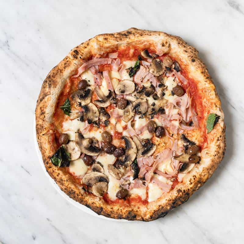 Capricciosa pizza topped with fior di latte, San Marzano tomato, ham, mushrooms, black olives, and fresh basil