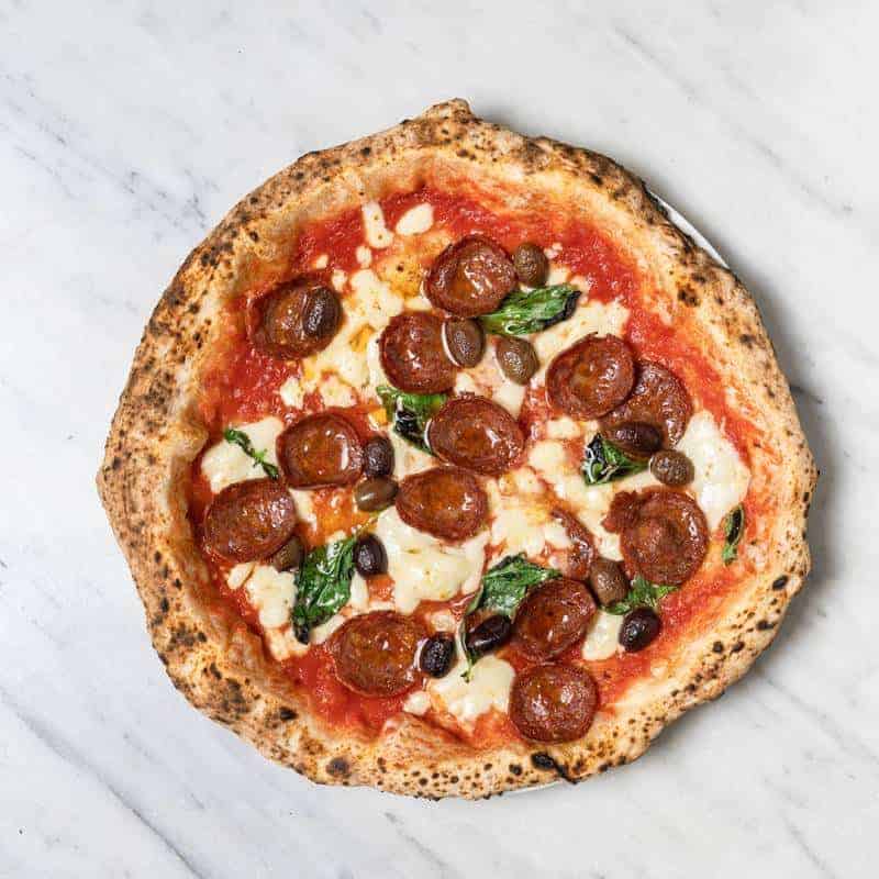 Spicy Diavola pizza topped with Solania San Marzano tomatoes, Fior di Latte, hot salami, Gaeta black olives, Pecorino Romano, basil, and EVOO at Via Napoli