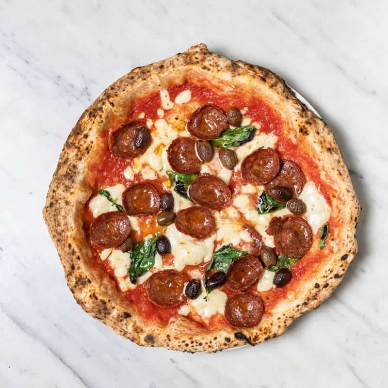 Spicy Diavola pizza topped with fior di latte, hot salami, San Marzano tomato, black olives, and fresh basil