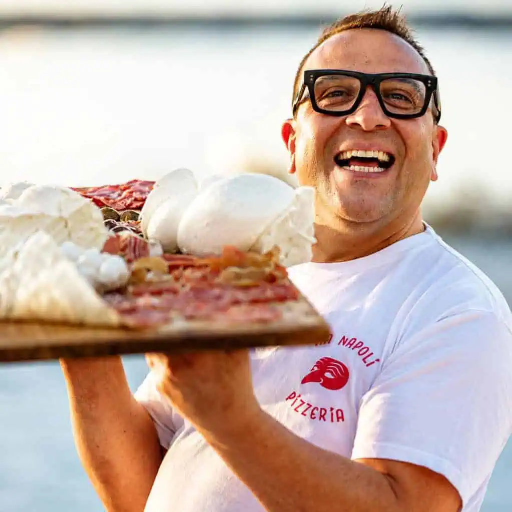 Luigi Esposito from Via Napoli holds a wooden pizza peel with wood-fired Neapolitan pizza and fresh mozzarella.