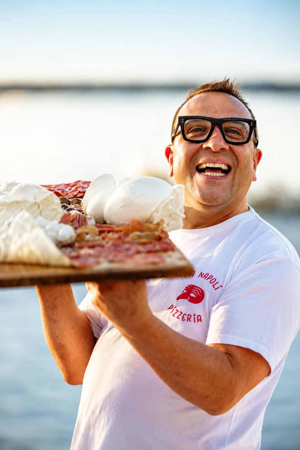 Luigi Esposito from Via Napoli holds a wooden pizza peel with wood-fired Neapolitan pizza and fresh mozzarella.