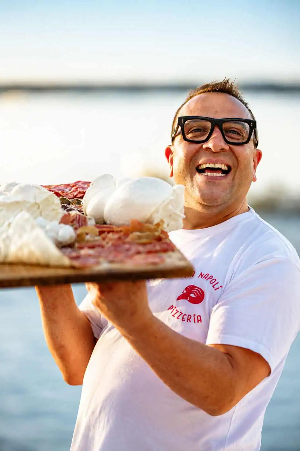 Luigi Esposito from Via Napoli holds a wooden pizza peel with wood-fired Neapolitan pizza and fresh mozzarella.
