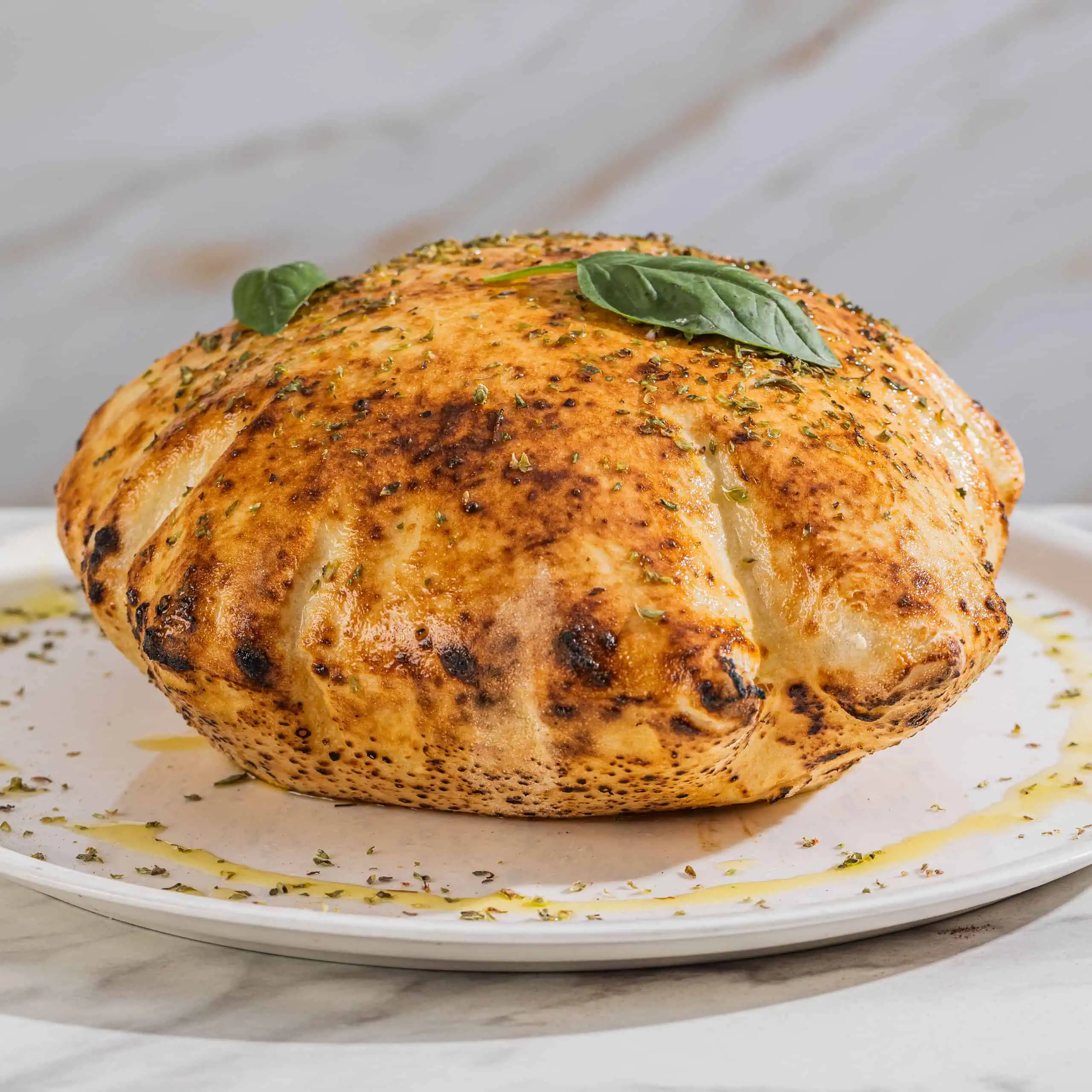 Wood-fired Panuozzo bread topped with herbs and drizzled with extra virgin olive oil at Via Napoli