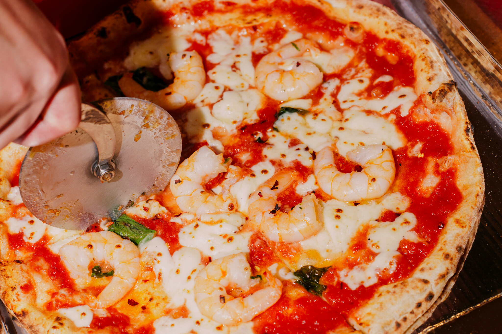 Hand slicing a fresh pizza with melted mozzarella and tomato sauce at Via Napoli Pizzeria