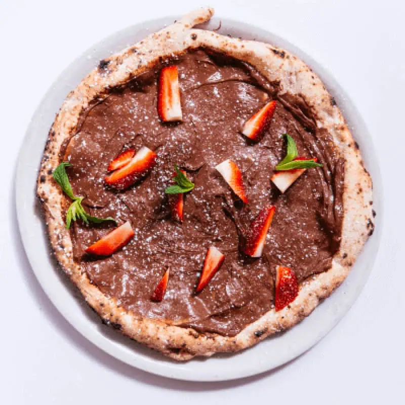 Dessert pizza smothered in creamy Nutella, topped with fresh strawberry slices and mint leaves, served at Via Napoli