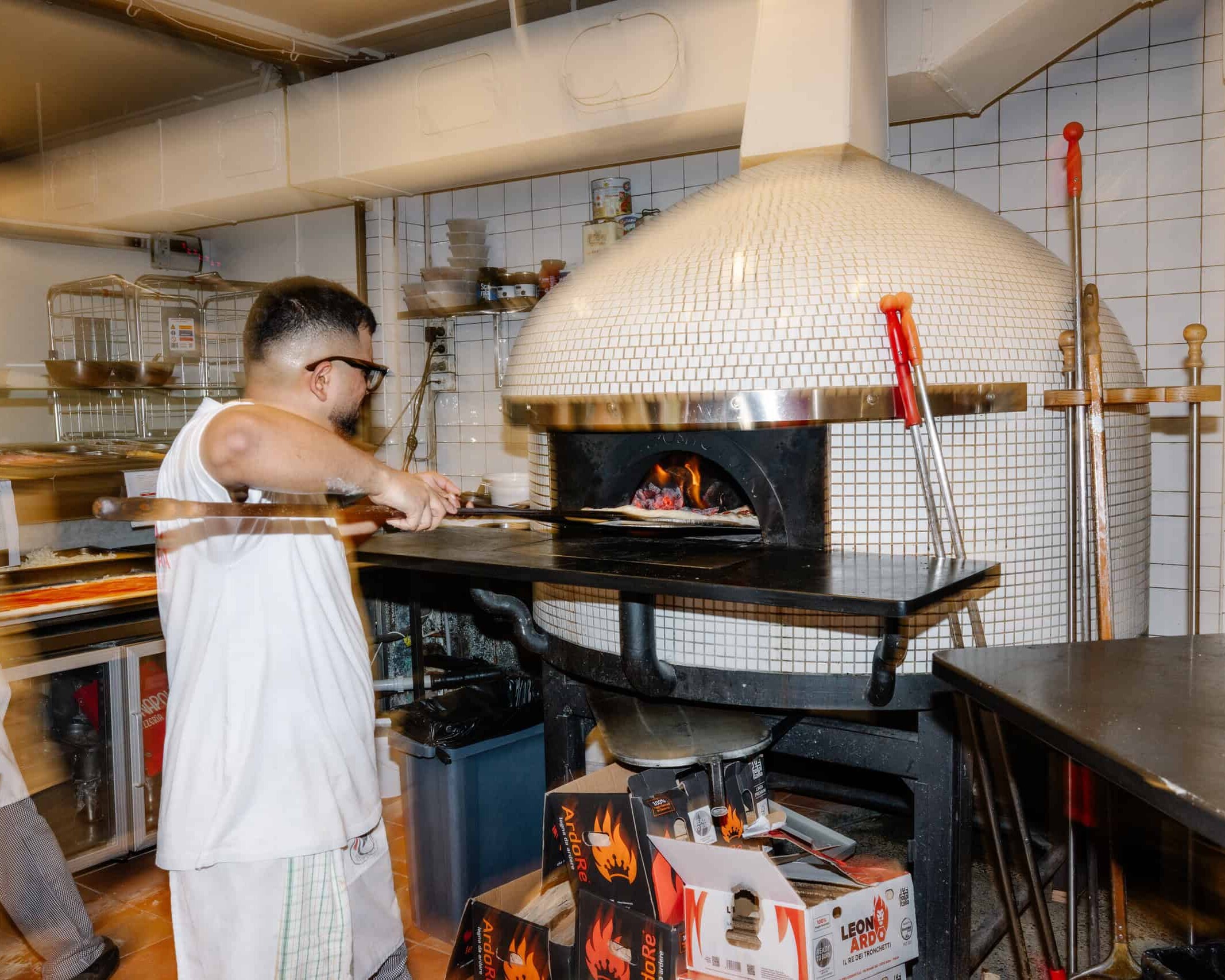 A pizzaiolo slides a pizza into a wood-fired mosaic dome oven at Vai Napoli restaurant.