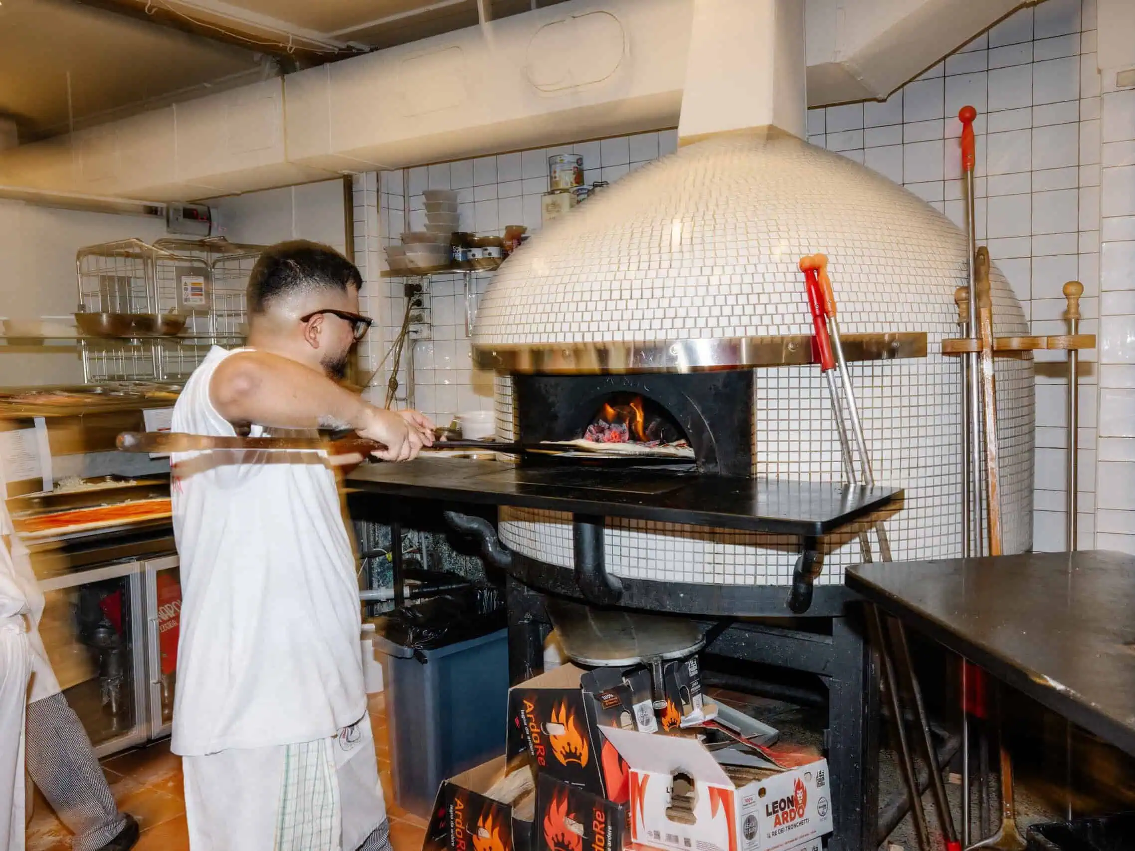 A pizzaiolo slides a pizza into a wood-fired mosaic dome oven at Vai Napoli restaurant.