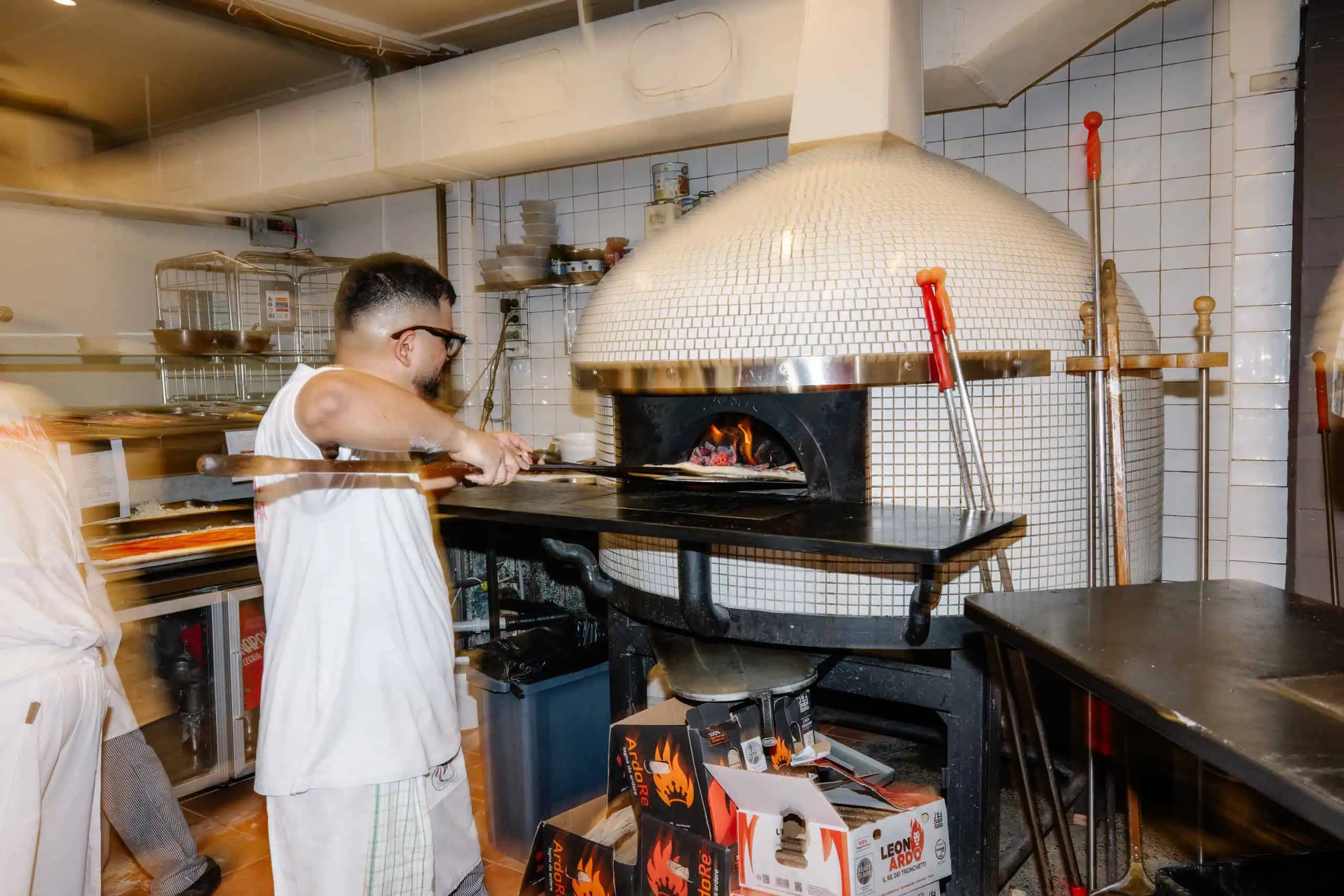 A pizzaiolo slides a pizza into a wood-fired mosaic dome oven at Vai Napoli restaurant.