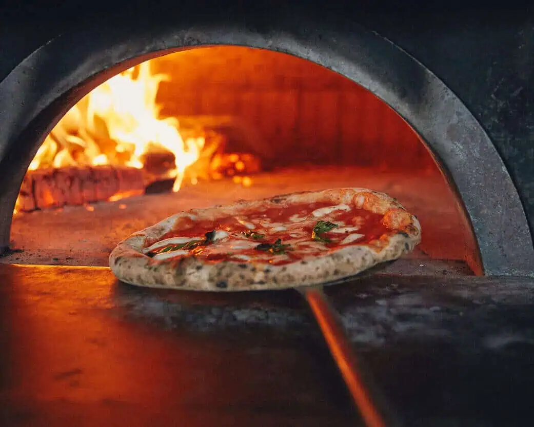 Removing Neapolitan pizza from wood-fired oven Via Napoli