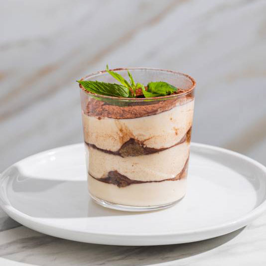 Traditional tiramisù dessert layered with espresso-soaked ladyfingers and mascarpone cream, served in a glass and garnished with fresh mint at Via Napoli