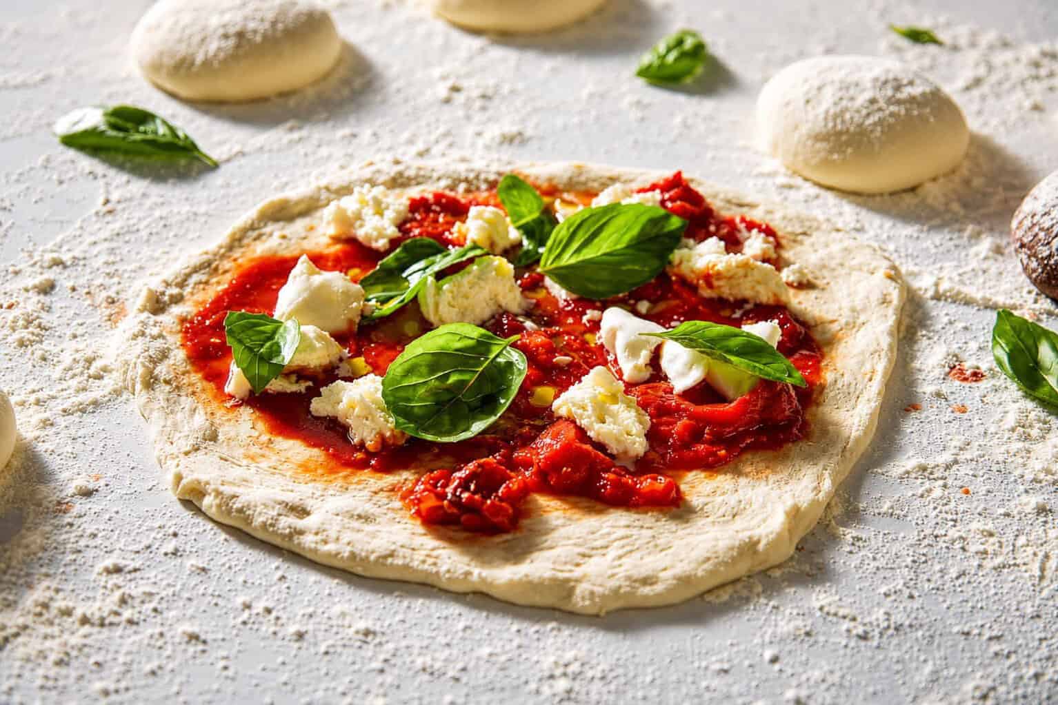 Uncooked Margherita pizza preparation fresh dough and basil