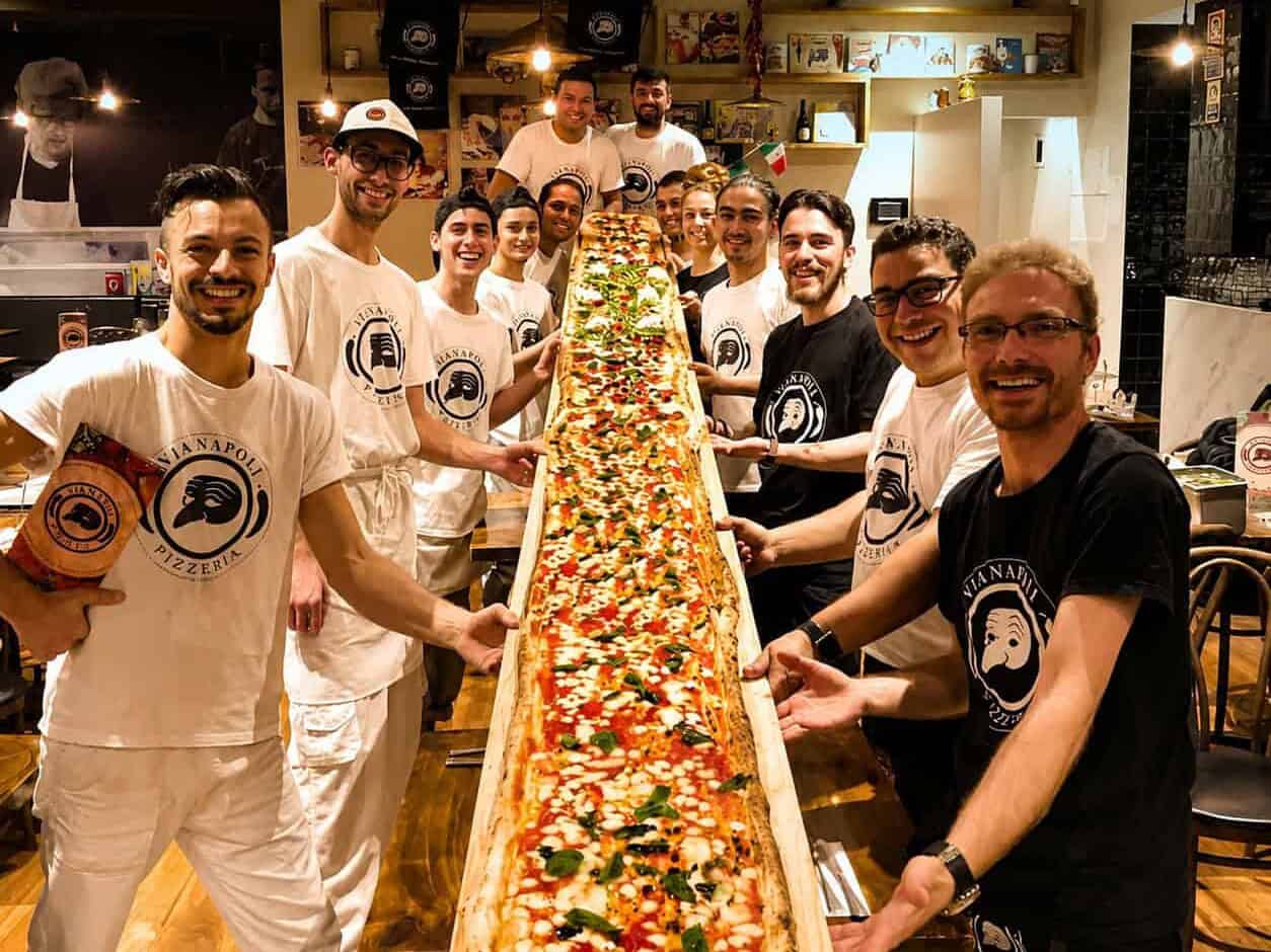 Group of Via Napoli staff and diners holding a 5-metre long giant pizza during the Via Napoli pizza challenge inside the restaurant