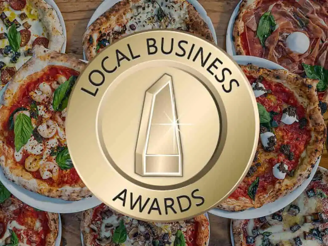 Local Business Awards emblem over a table filled with a variety of gourmet wood-fired pizzas from Via Napoli Pizzeria.