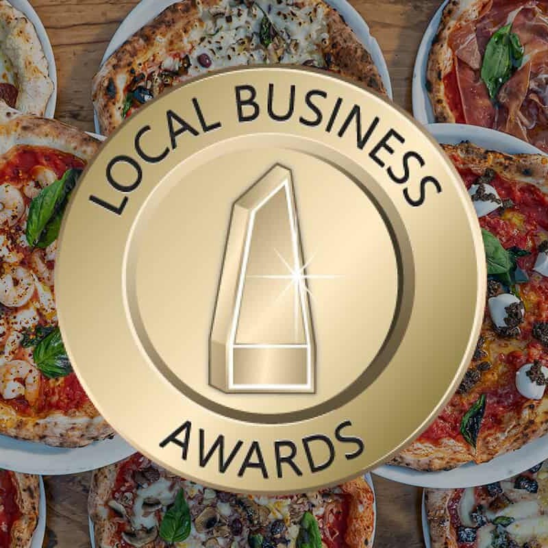 Local Business Awards emblem over a table filled with a variety of gourmet wood-fired pizzas from Via Napoli Pizzeria.
