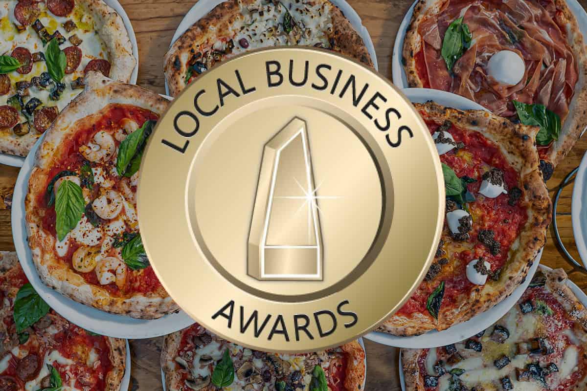 Local Business Awards emblem over a table filled with a variety of gourmet wood-fired pizzas from Via Napoli Pizzeria.