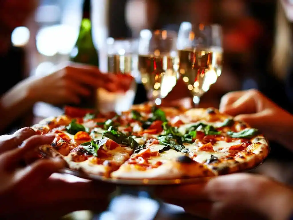 Friends enjoying a wood-fired pizza and toasting with champagne at a lively restaurant gathering