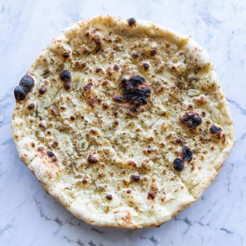 Close-up of woodfired pizza crust topped with garlic, oregano, olive oil or melted buffalo mozzarella